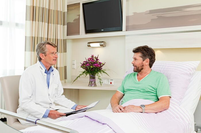 Patient im Krankenhausbett spricht mit Arzt, der neben ihm sitzt