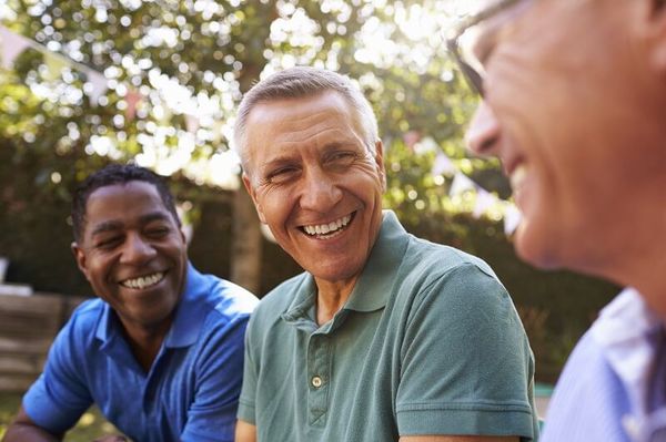 drei Männer mittleren Alters lachen im Garten miteinander